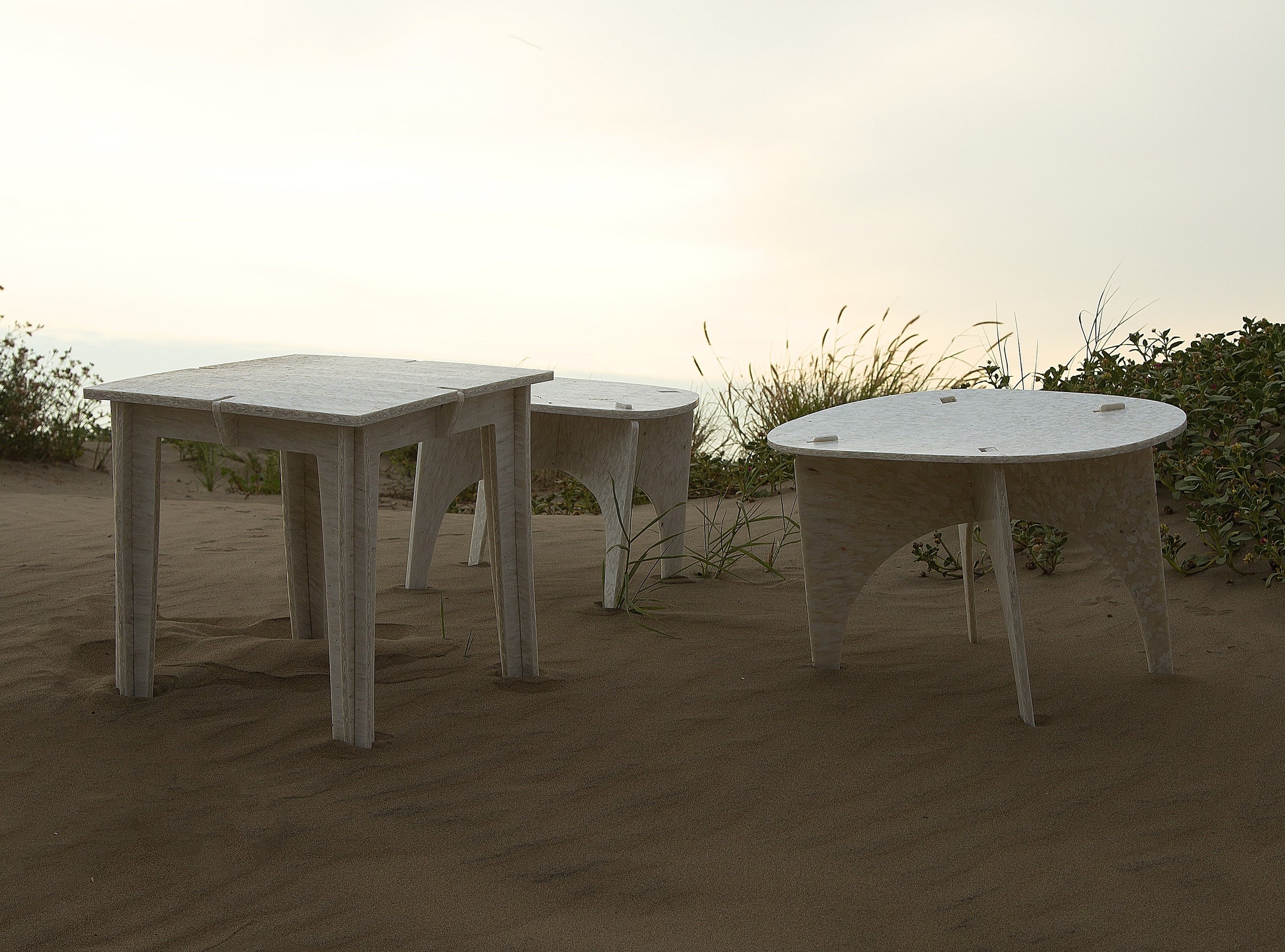 Three furniture tables on a sandy beach overlooking the ocean.
